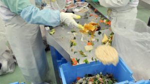 Varios empleados de la planta de reciclaje de alimentos Agri Gaia System Co. Ltd. separan la comida pasada de fecha