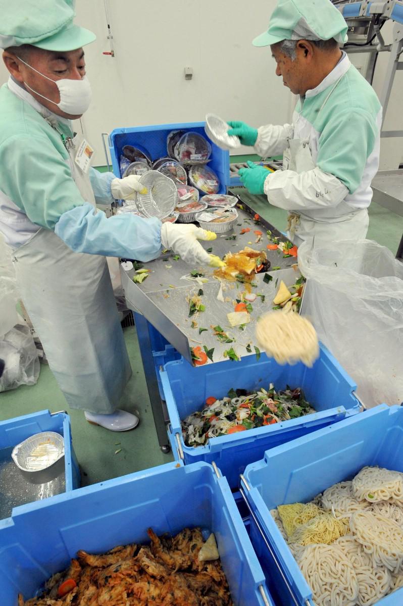 Varios empleados de la planta de reciclaje de alimentos Agri Gaia System Co. Ltd. separan la comida pasada de fecha