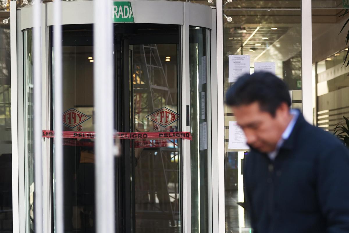 Una persona camina frente a la puerta de acceso al edificio de YPFB