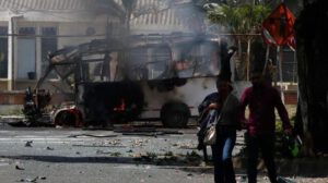 Personas caminan frente a un vehículo afectado por una explosión