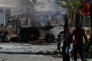 Personas caminan frente a un vehículo afectado por una explosión