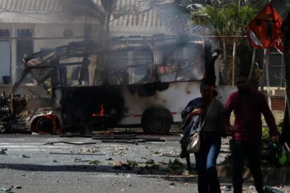 Personas caminan frente a un vehículo afectado por una explosión