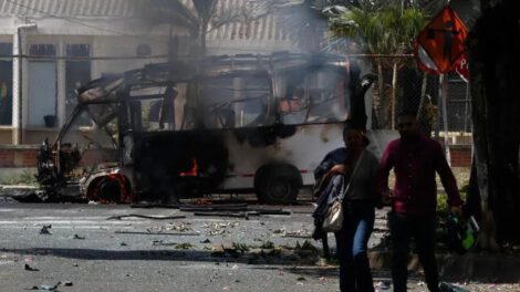 Personas caminan frente a un vehículo afectado por una explosión