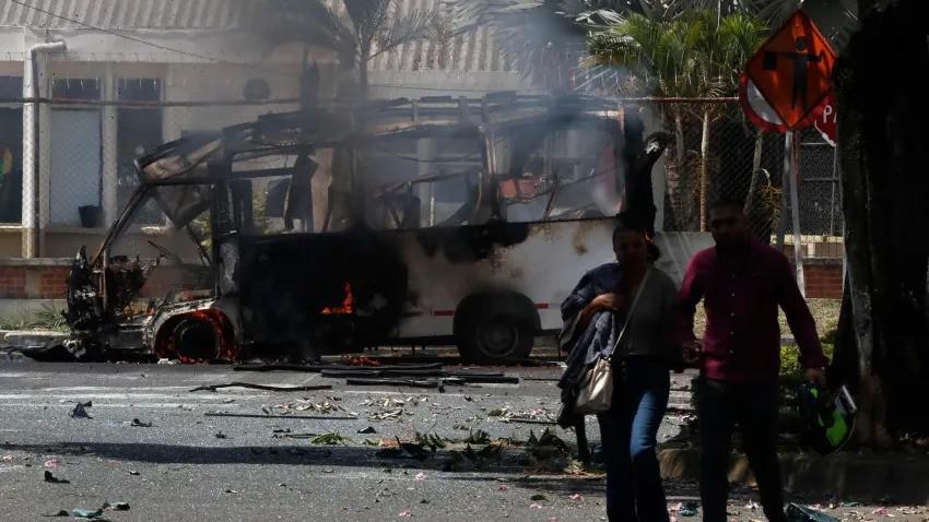 Personas caminan frente a un vehículo afectado por una explosión