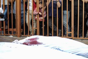 Un niño palestino observa tras unos barrotes los cadáveres de las víctimas cubiertos con sabana