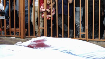 Un niño palestino observa tras unos barrotes los cadáveres de las víctimas cubiertos con sabana