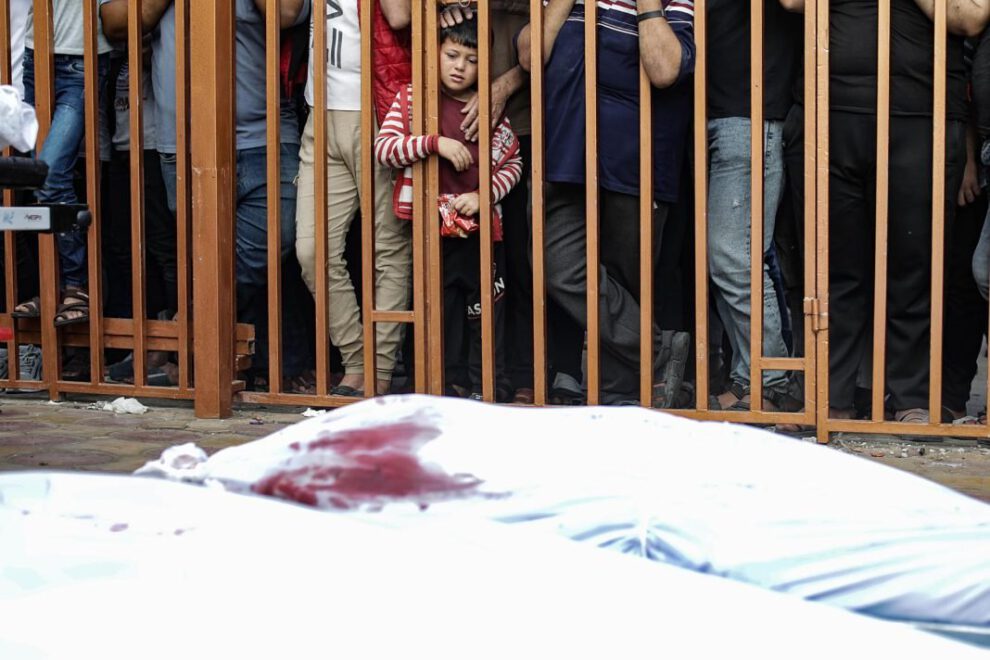 Un niño palestino observa tras unos barrotes los cadáveres de las víctimas cubiertos con sabana