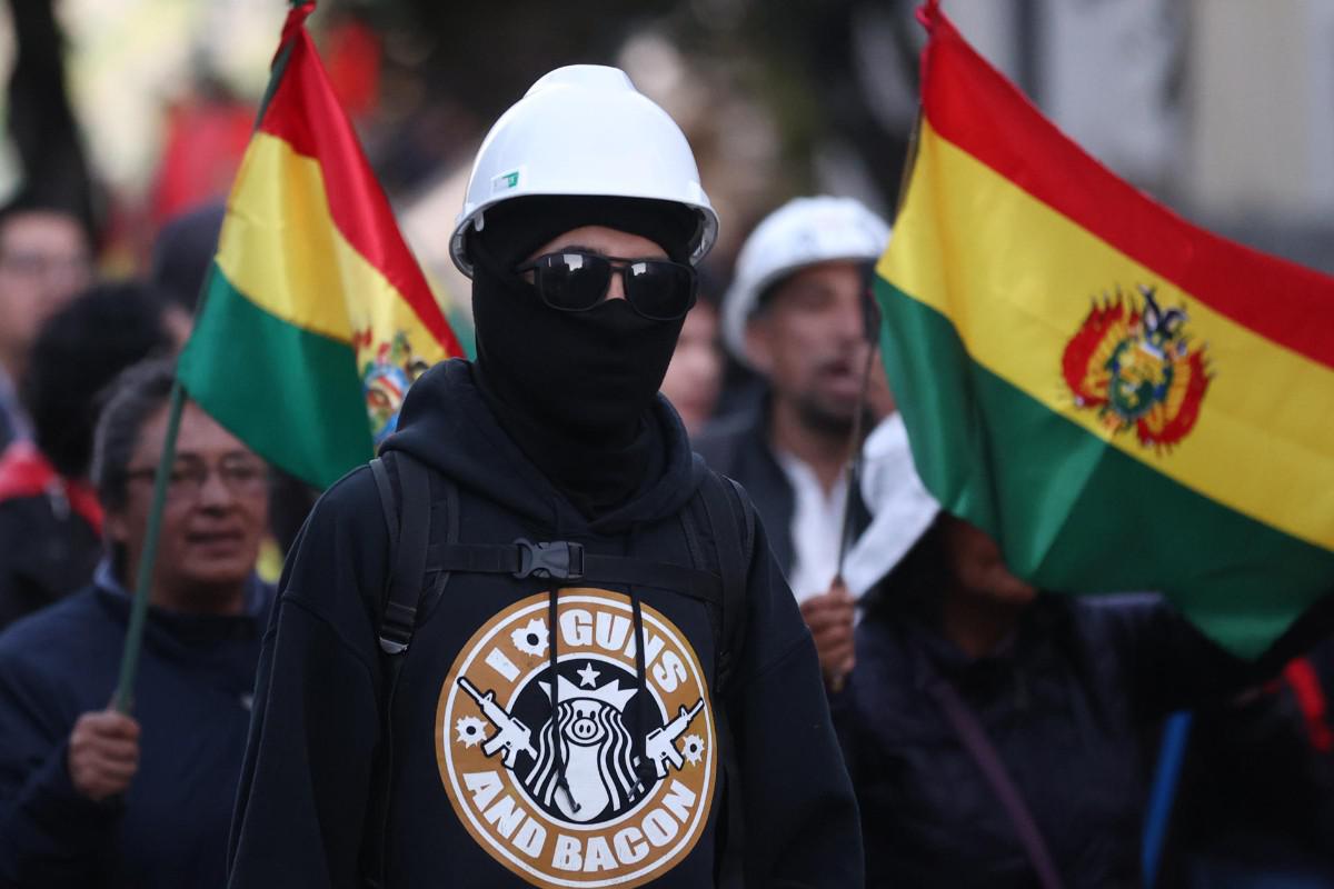 Un manifestante con el rostro cubierto y casco de seguridad porta banderas bolivianas durante la movilización