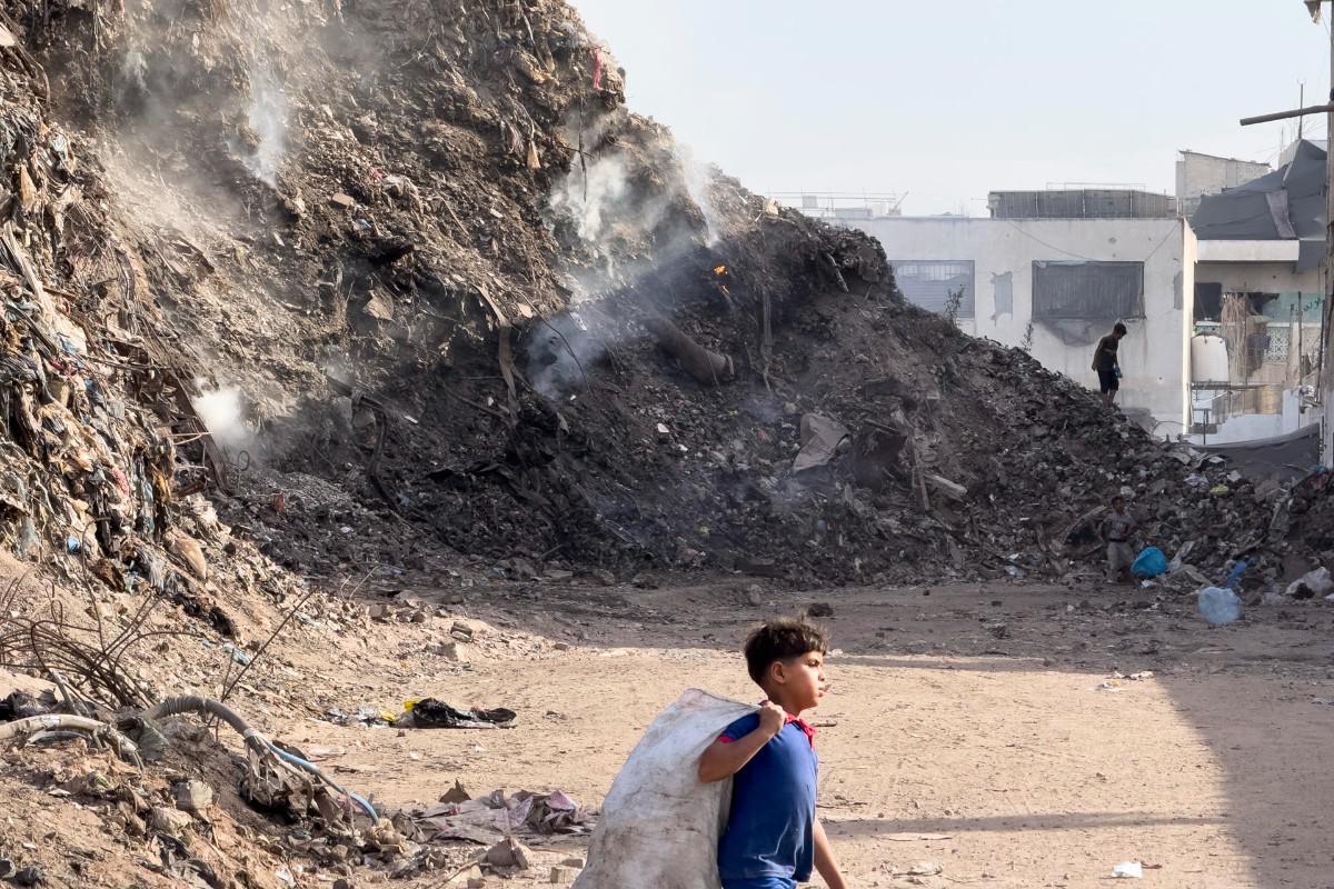 Un niño camina junto a una montaña de basura y escombros