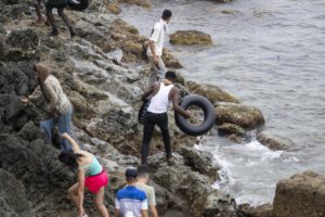 Migrantes usando flotadores caseros para cruzar por la zona rocosa de la costa