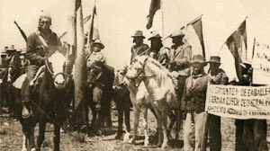 Cammpesinos a caballo y a pie portando banderas