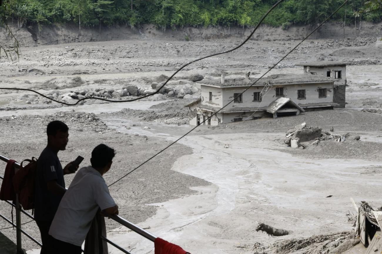 Varias personas observan cómo las aguas de la inundación arrasan Trishuli Bazar