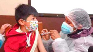 Un niño con barbijo recibiendo una vacuna en el brazo por parte de una enfermera