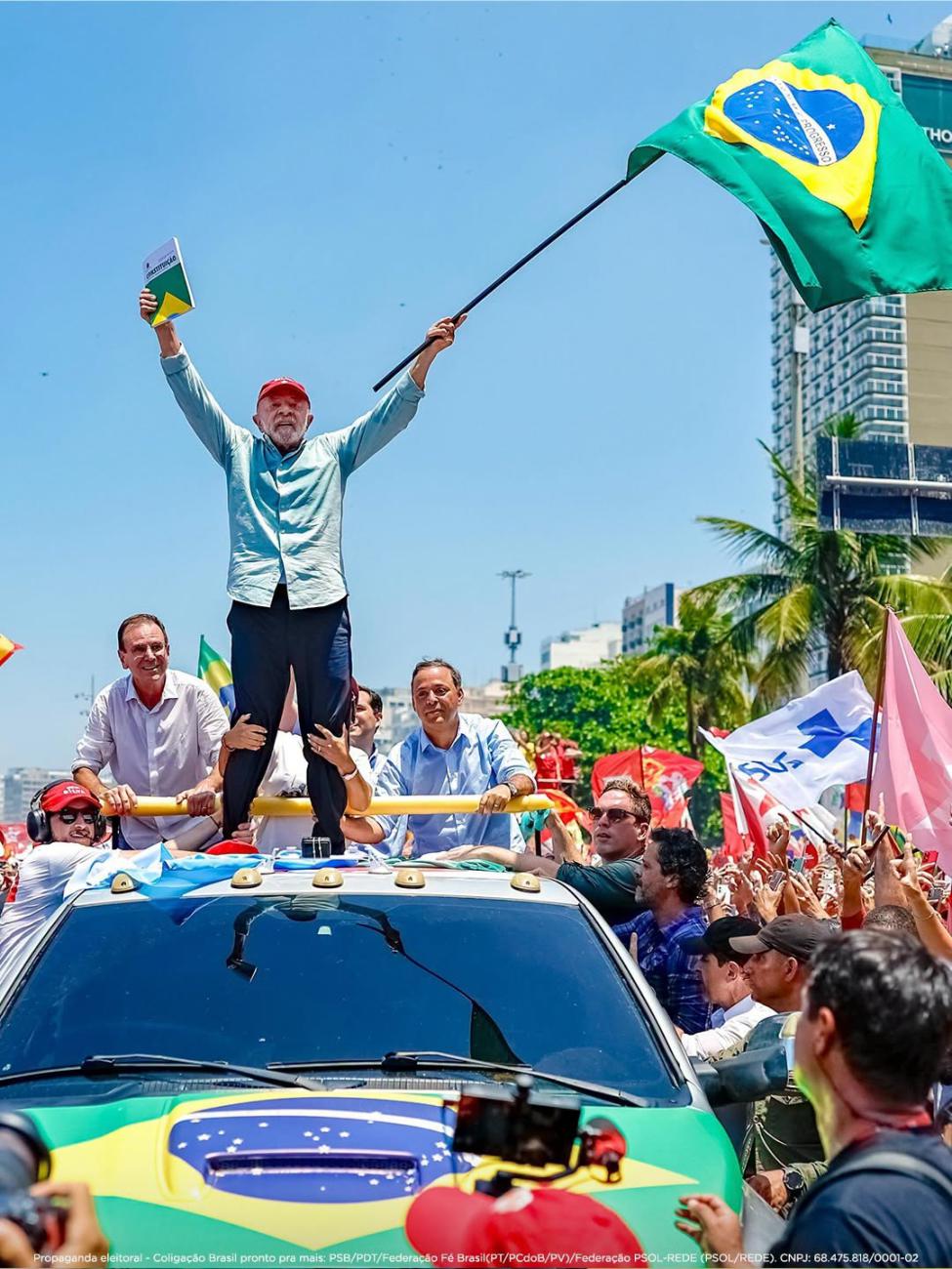 Lula da Silva se eleva sobre un vehículo sosteniendo un ejemplar de la Constitución y la bandera de Brasil