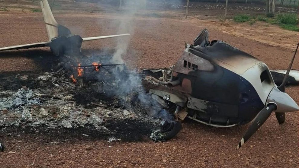 Restos quemados y humeantes de una avioneta monomotor destruida en un terreno de tierra rojiza